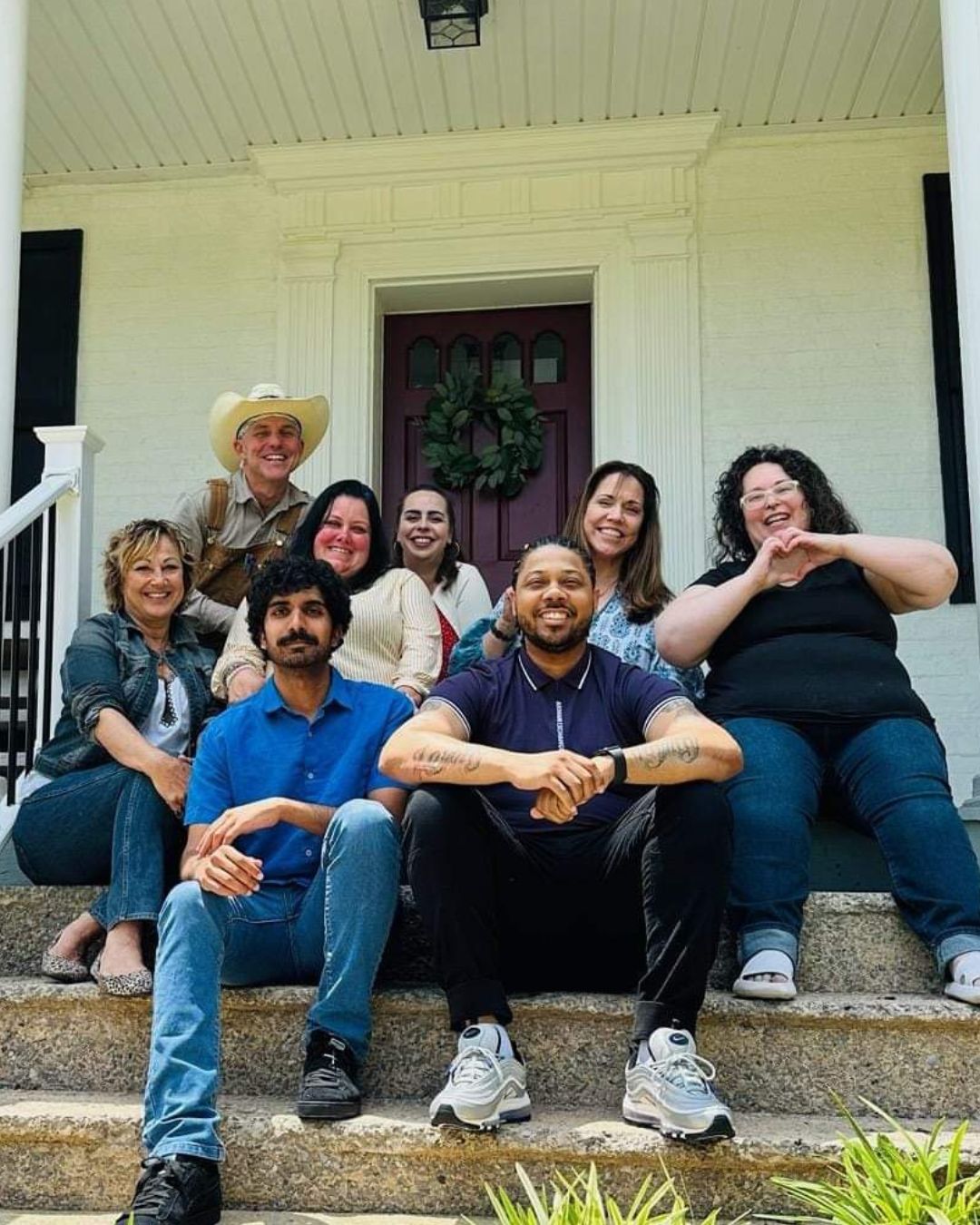 daytime color photo of adult Steadfast staff members sitting on front steps of Steadfast house 2023