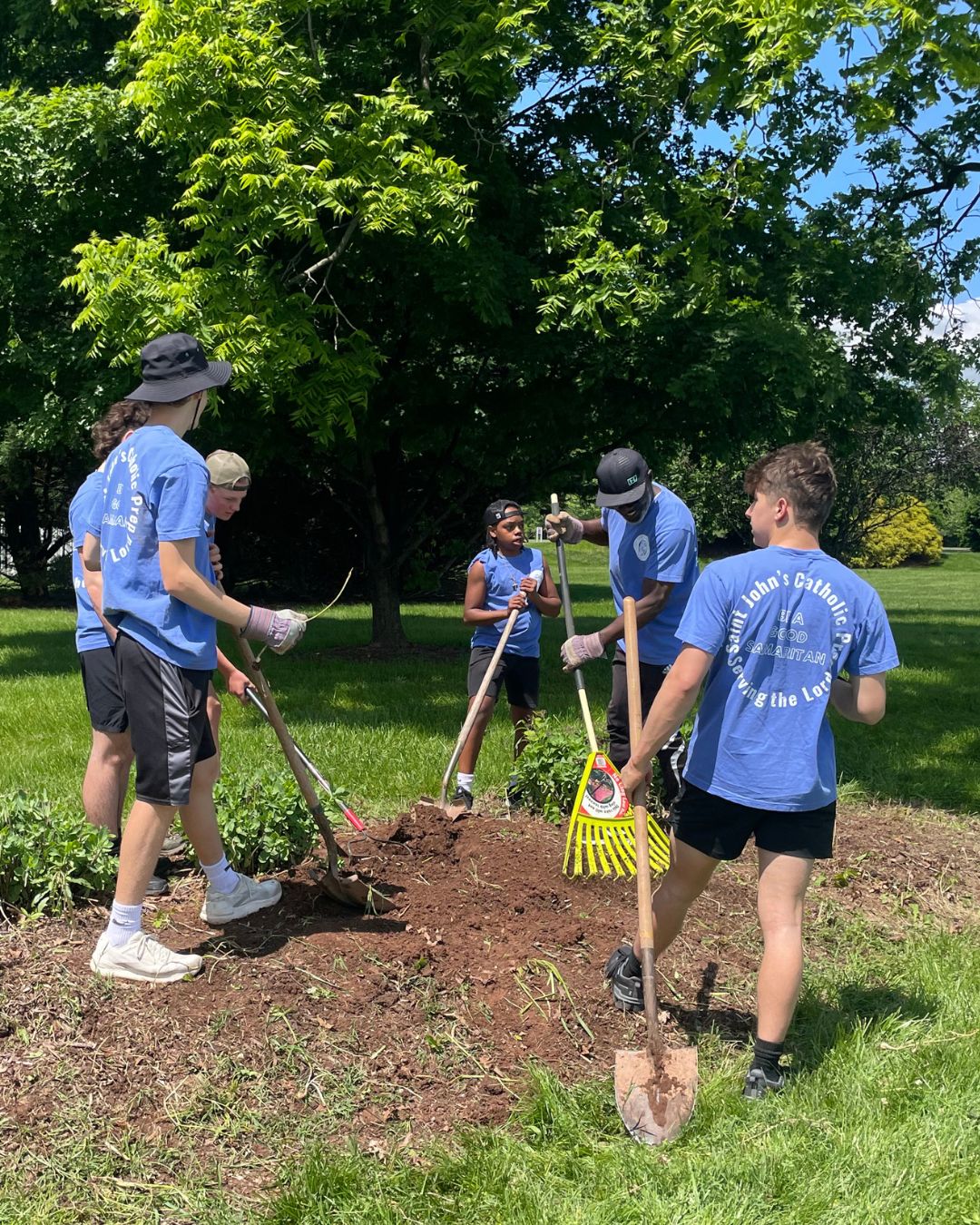 daytime color photo of youth volunteers with garden equipment working in Steadfast yard on a sunny day