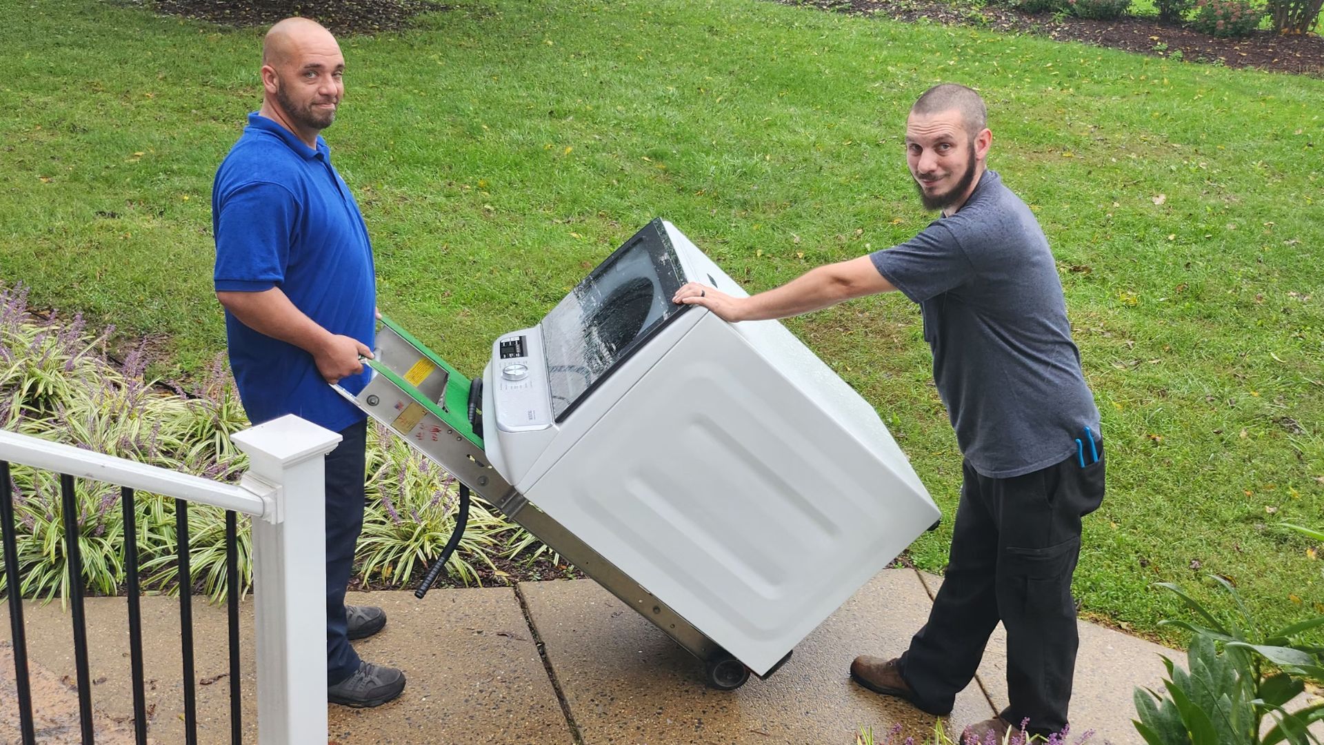 2 men outside the front steps delivering a new washing machine on a handtruck to the Steadfast house