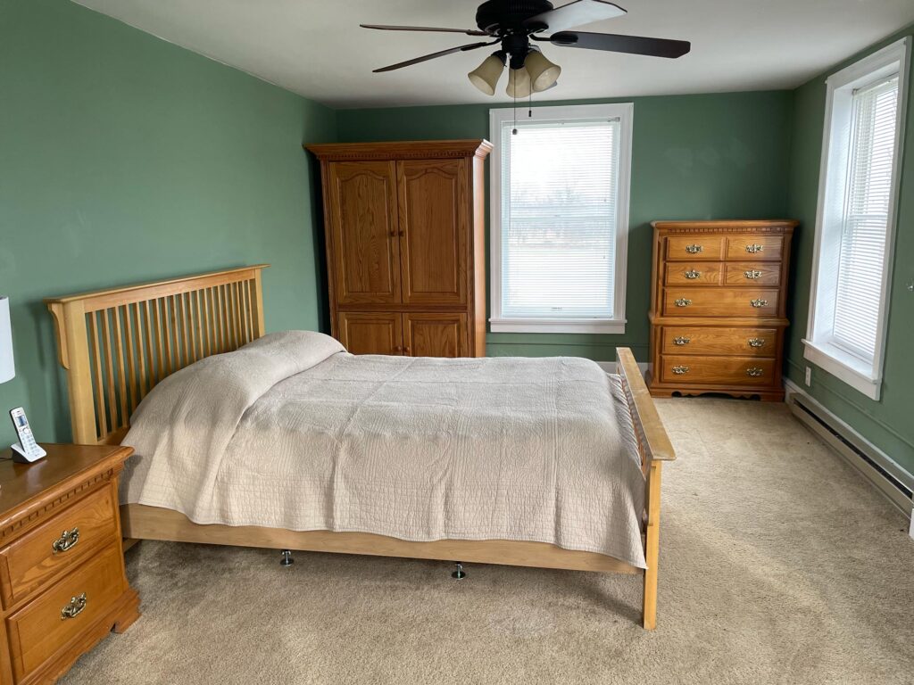 bed in a carpeted room with ceiling fan, night stand, & dressers