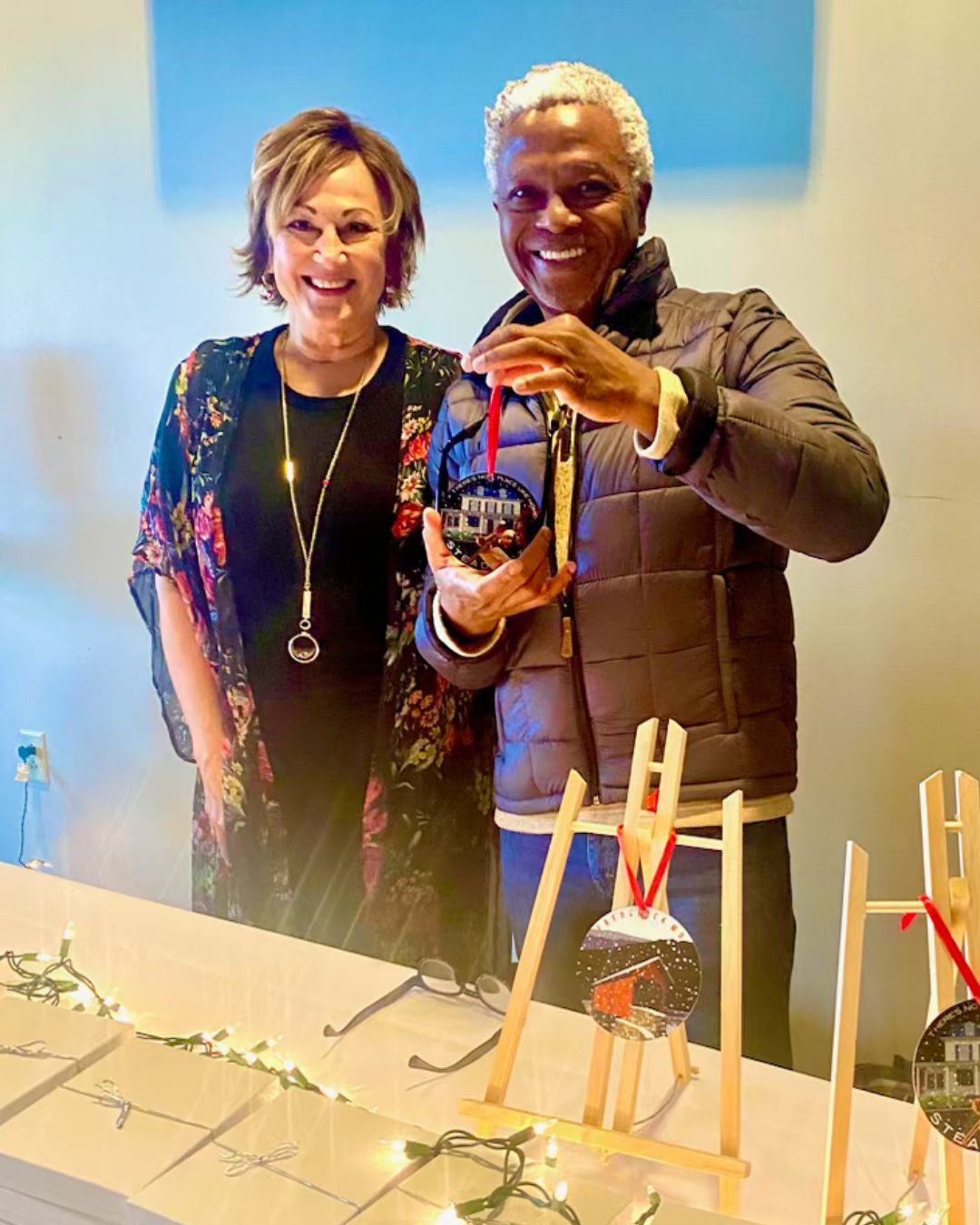 photo of Steadfast executive director Cindy Morgan and artist Yemi with Yemi Christmas ornaments on a table in front of them