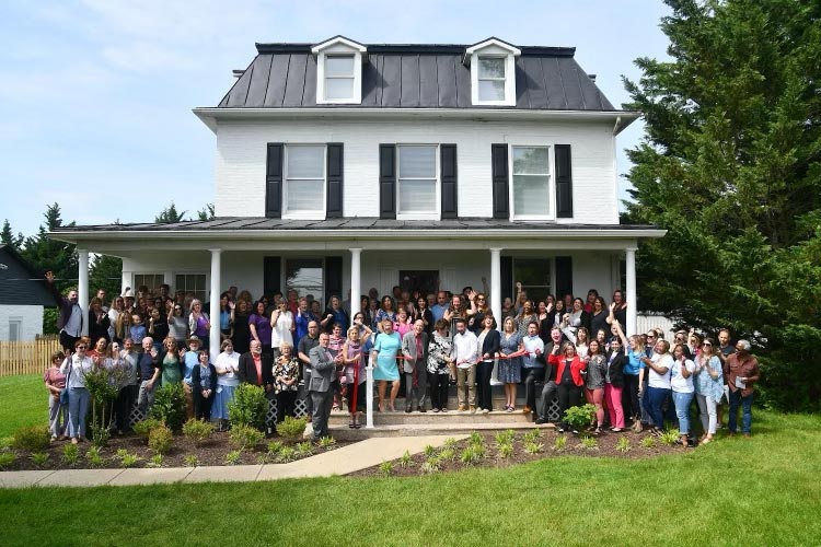 Outdoor photo of dozens of people on Steadfast home's front porch, steps, and yard for the 2023 ribbon-cutting and open house