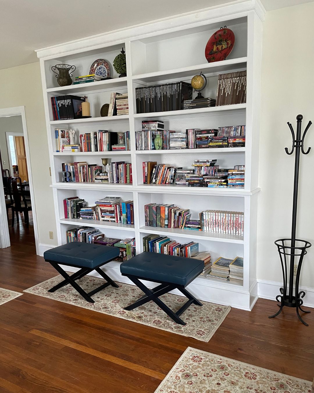 White built-in bookshelves in a library with area rugs on wooden floor, and leather covered settees