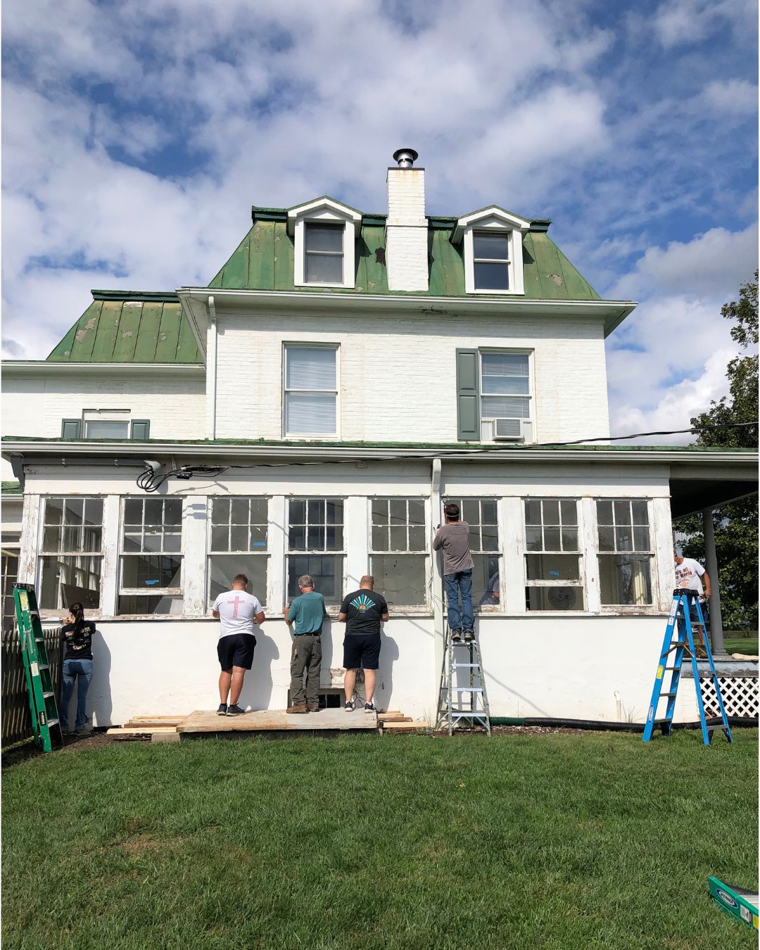 daytime color picture of 6 people, some on ladders, renovating the Steadfast farmhouse for future residency
