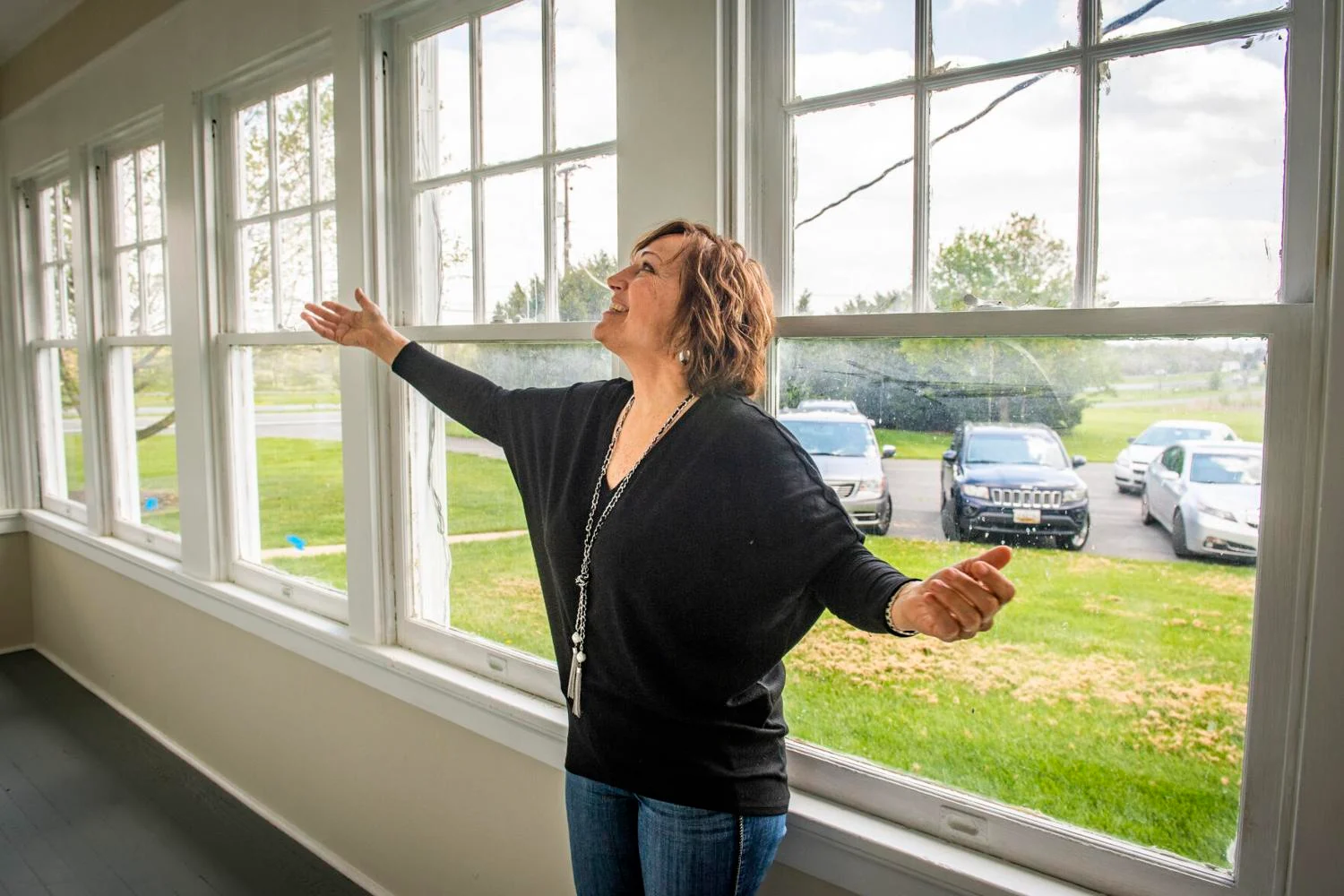photo of executive director Cindy Morgan looking up with her arms spread wide in thanks in the newly renovated sunroom of the Steadfast farmhouse