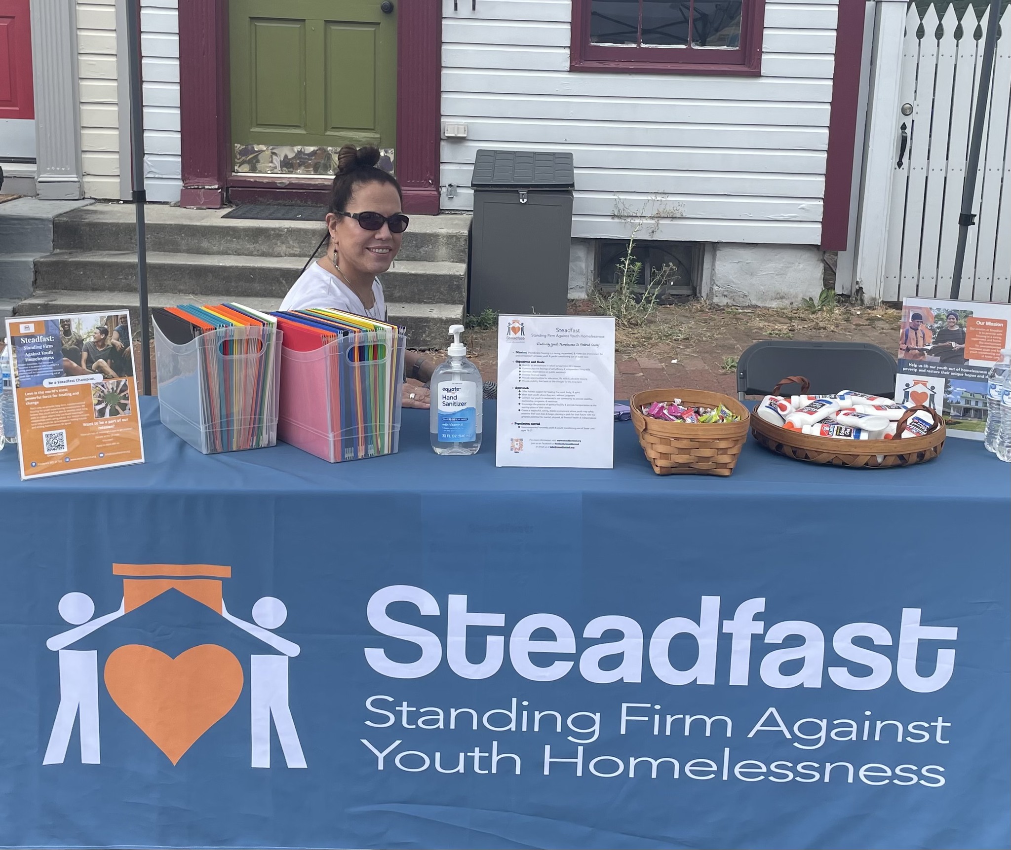 Color photo of marketing and events coordinator Susan Futran sitting behind the Steadfast table at In the Streets Festival 2025